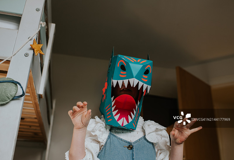 一个戴着自制纸板恐龙面具的孩子，摆出凶猛的姿势，朝着镜头咆哮图片素材