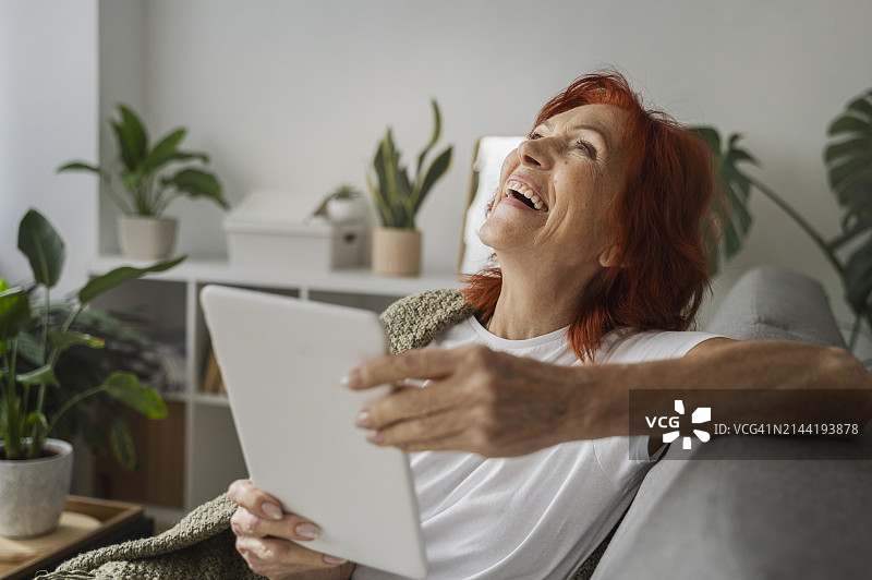 在家中客厅里用平板电脑欢笑的老年妇女图片素材
