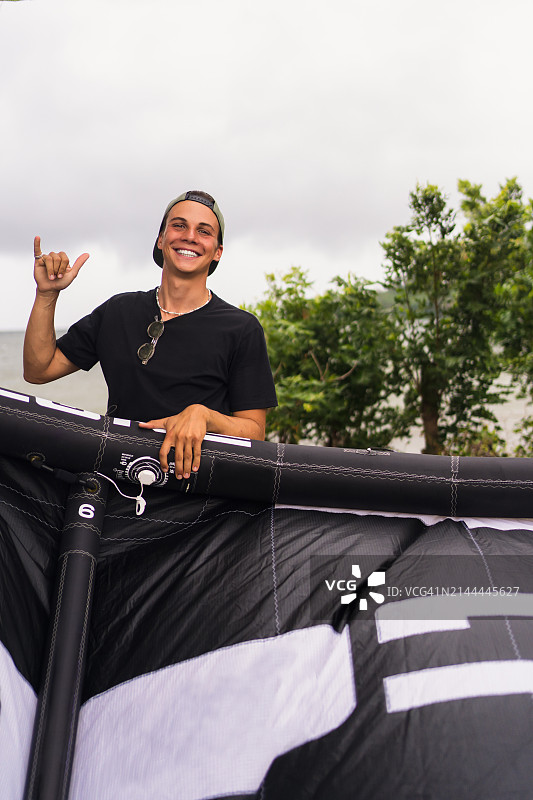 年轻的金发风筝冲浪者对着镜头微笑，并致以冲浪者的问候，容光焕发图片素材