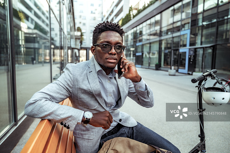 穿着得体的年轻男商人在城市的长椅上讲智能手机图片素材