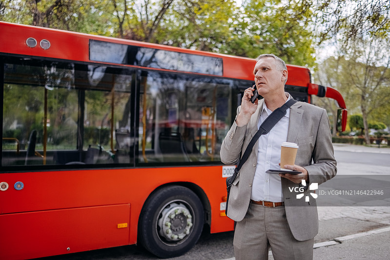 在户外使用通讯设备等待交通工具的商务人士图片素材
