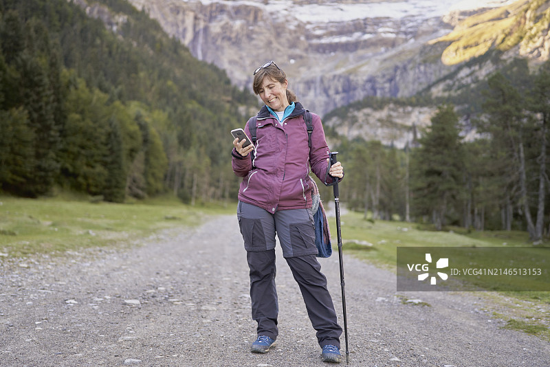 穿着运动服、背着背包站在土路上，拿着手机用登山杖自拍的女人图片素材