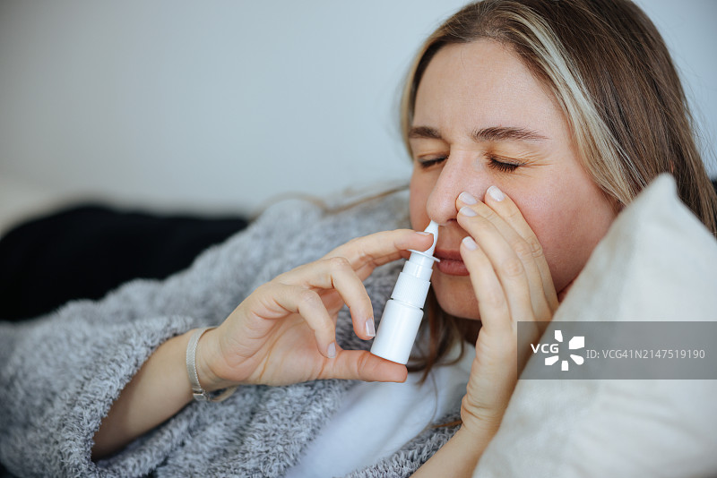 生病的年轻女人使用鼻腔喷雾剂图片素材