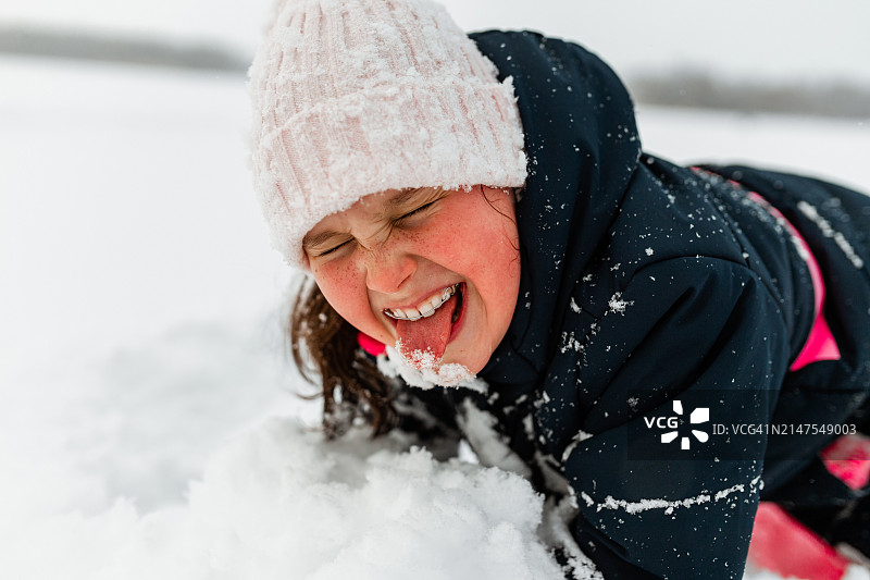快乐的女孩眯着眼睛，吐着舌头，倒在雪堆里图片素材