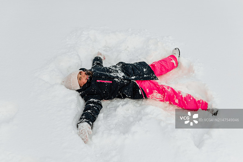 年轻女孩躺在雪地里做雪天使图片素材