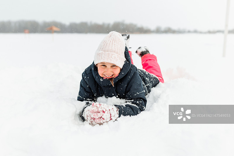 小女孩趴在雪地里，面带笑容图片素材