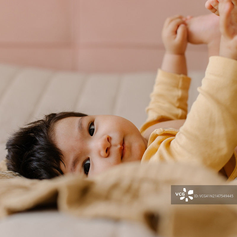 可爱的亚洲女婴身穿连体衣躺在米色格子床上，展现宝宝的成长与发展图片素材