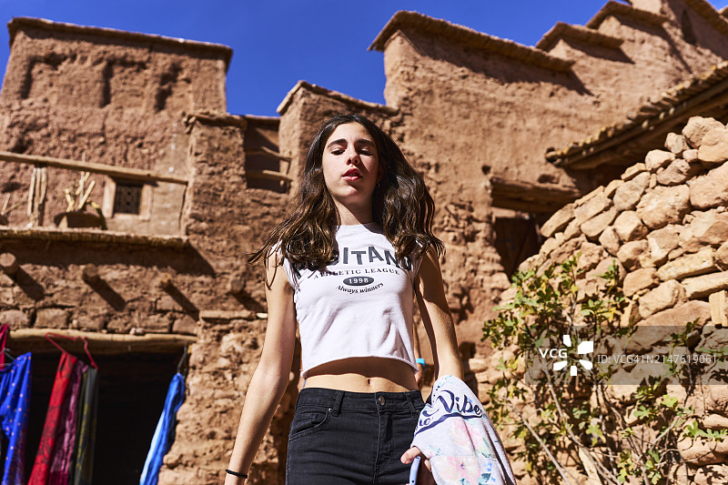 一位年轻女子走在摩洛哥艾本哈杜村的土墙后面，向下看。图片素材