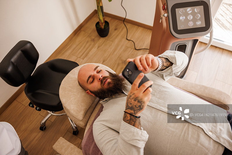 在美容院做完护理后用手机自拍的年轻络腮胡男子图片素材