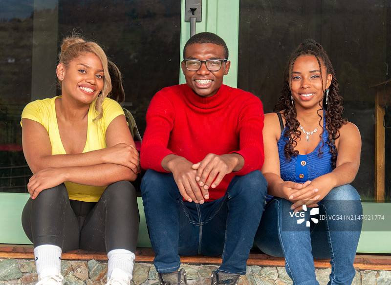 三个朋友在门廊上亲密地坐在一起，笑容温暖，姿态放松，洋溢着友谊的幸福图片素材