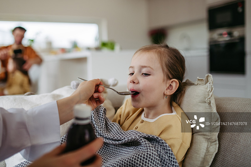 女孩生病发烧头痛，母亲喂女儿吃药，勺子里装着止咳糖浆。母亲节和母爱概念图片素材
