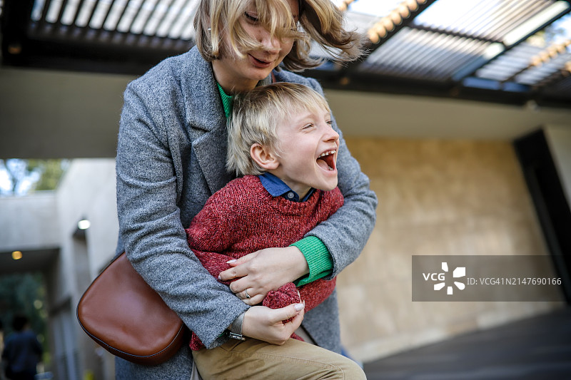 温馨时刻：中年母亲在城镇街道上拥抱穿着毛衣的儿子图片素材
