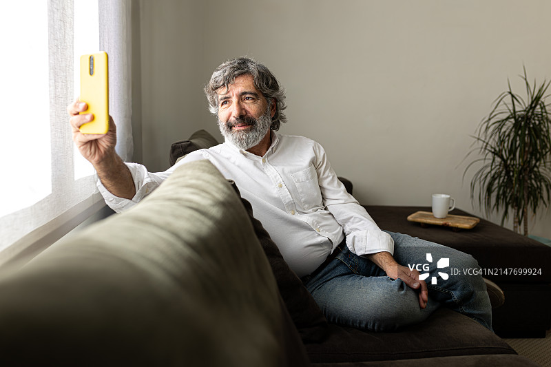 中年男人在家放松，用手机在沙发上自拍图片素材