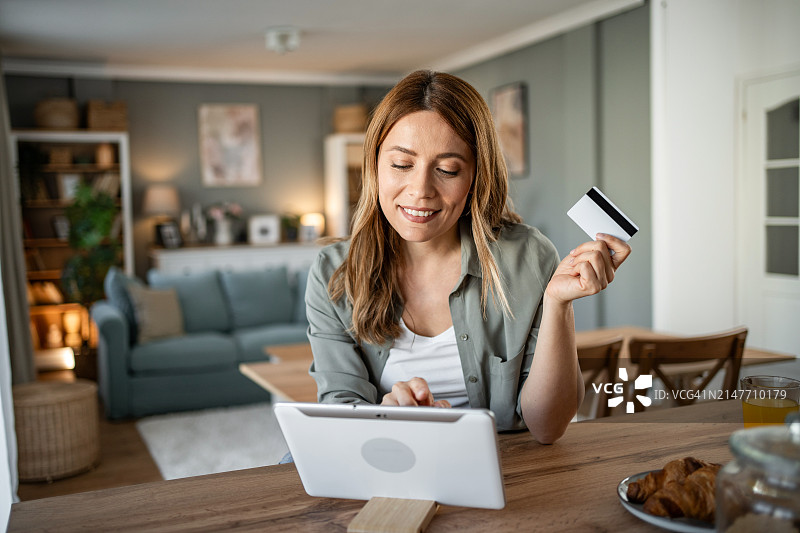 一名女子坐在房间里，通过平板电脑和信用卡在网上银行查看她的每月预算图片素材