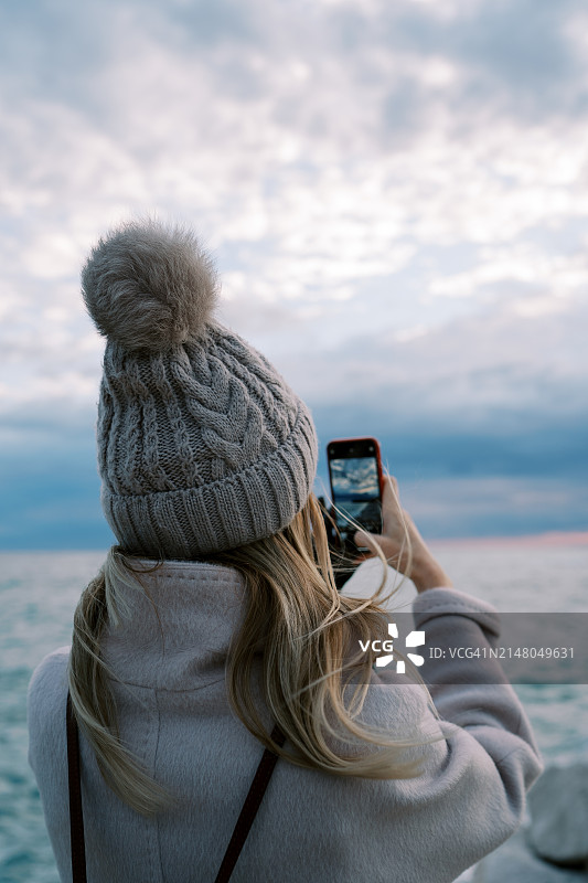 女孩站在岸边，用手机拍摄海上日落图片素材