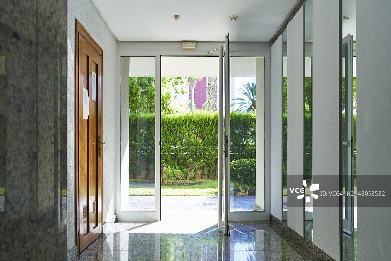 酒店走廊，玻璃门通向带草坪和灌木的庭院图片素材