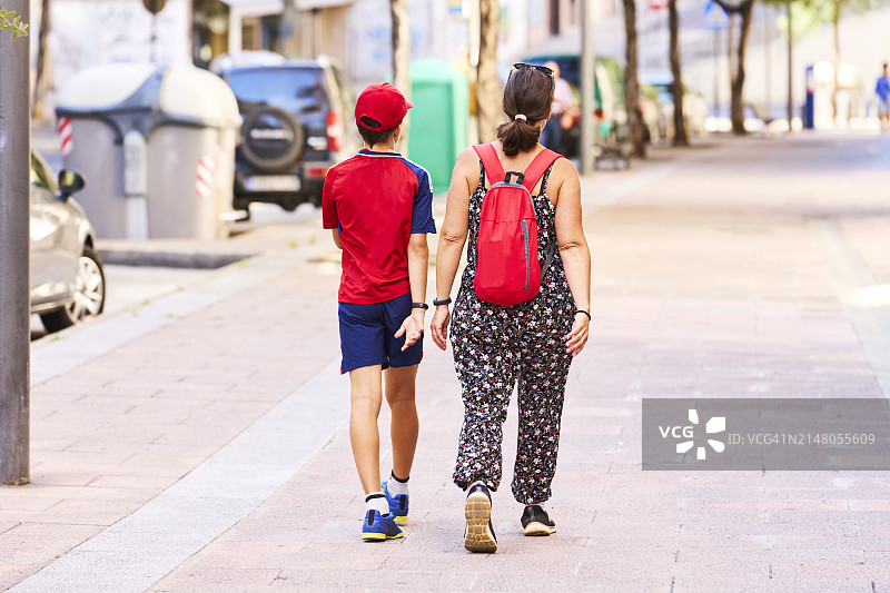 穿着休闲装，背着背包走在儿子旁边的街上的女人（后视图）图片素材