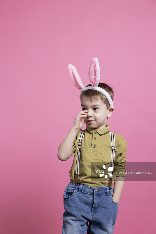 戴着兔子耳朵发带，背景为粉色的可爱男孩肖像图片素材