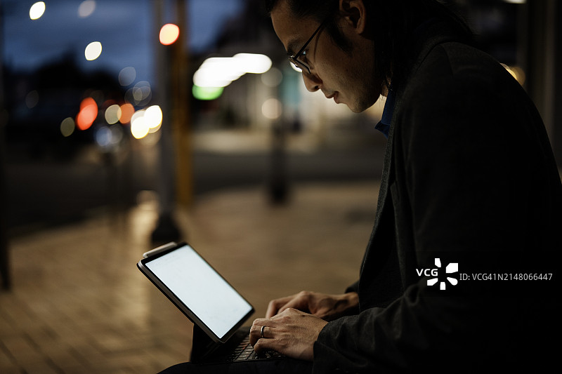 夜晚在街上用平板电脑打字的亚洲男人图片素材