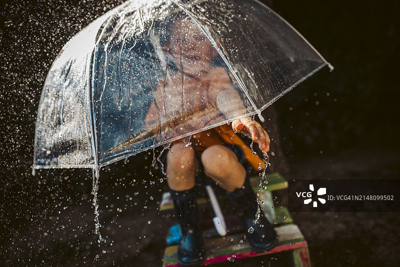 雨天概念：男孩蹲在伞下，接住从天空落下的雨滴图片素材