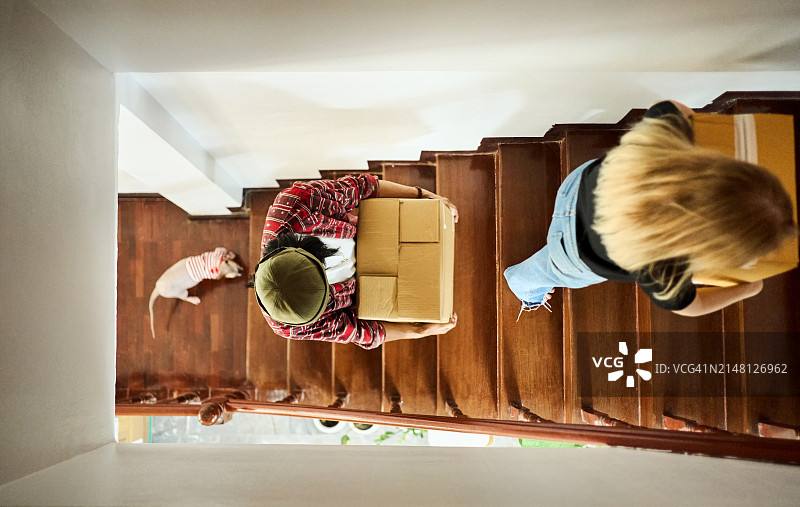 年轻夫妇搬着箱子在新房子里上楼图片素材