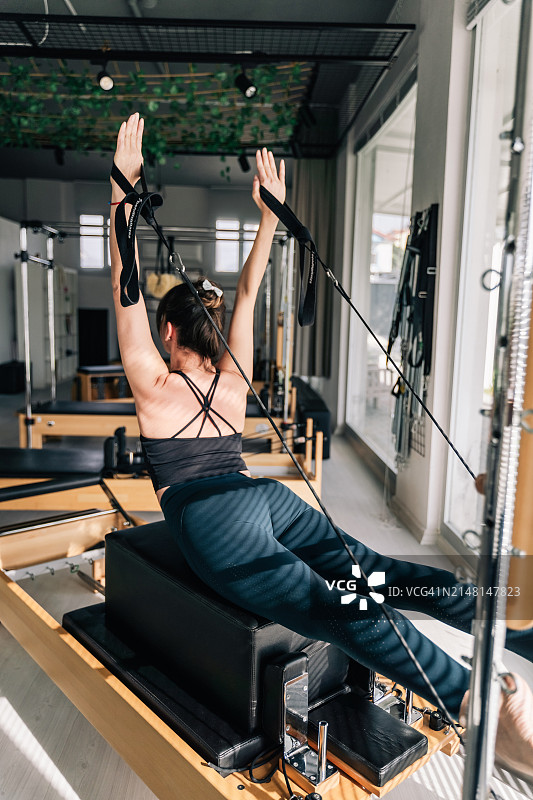 在阳光明媚的日子里，美丽的女子在器械上做普拉提运动图片素材