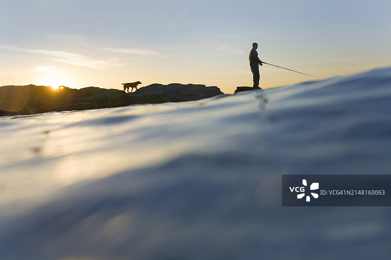 在岩石上钓鱼，带狗图片素材