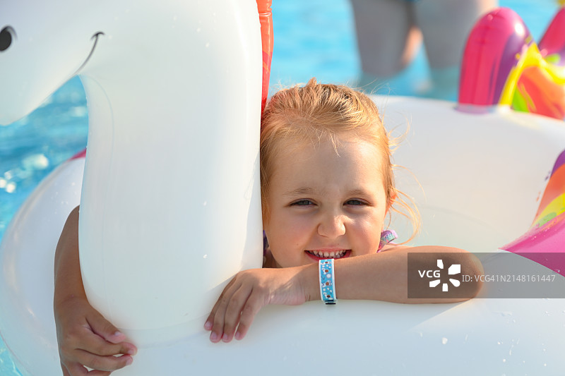 在游泳池中手持充气泳圈的微笑女孩肖像图片素材