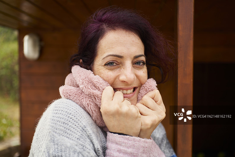 冬季：戴着围巾的白人女性在小屋外端着茶杯看向镜头图片素材