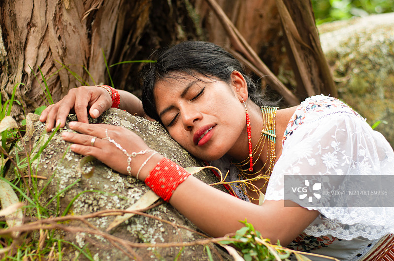 来自厄瓜多尔的少数民族妇女在树木和植被之间的岩石上休息，与大自然母亲联系，西班牙裔传统月图片素材
