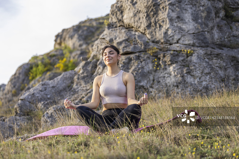 春日，山丘环绕的草地上冥想的年轻女孩侧视图图片素材