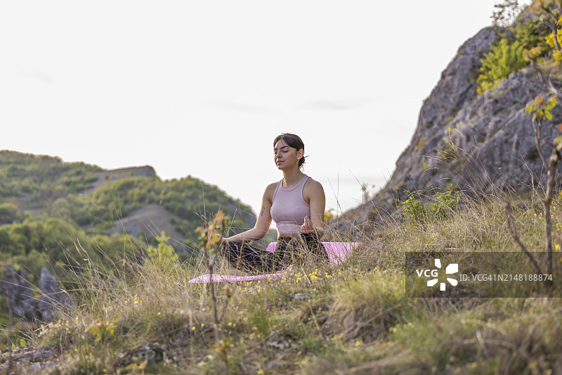 春日，山丘环绕的草地上冥想的年轻女孩侧视图图片素材