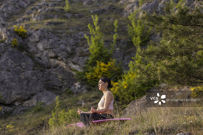 春日，山丘环绕的草地上冥想的年轻女孩侧视图图片素材