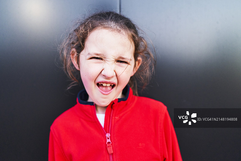 一个穿着毛衣的可爱女孩对着镜头微笑，做着鬼脸的正面照图片素材