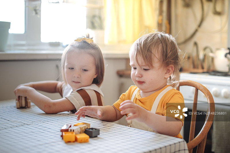 温馨的兄弟姐妹情：孩子们在厨房的桌旁玩环保木制玩具，安全又环保图片素材