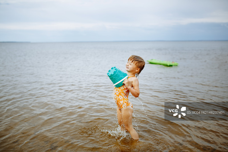 湖畔欢乐：兴奋的女孩在浅水中用水桶倒水图片素材