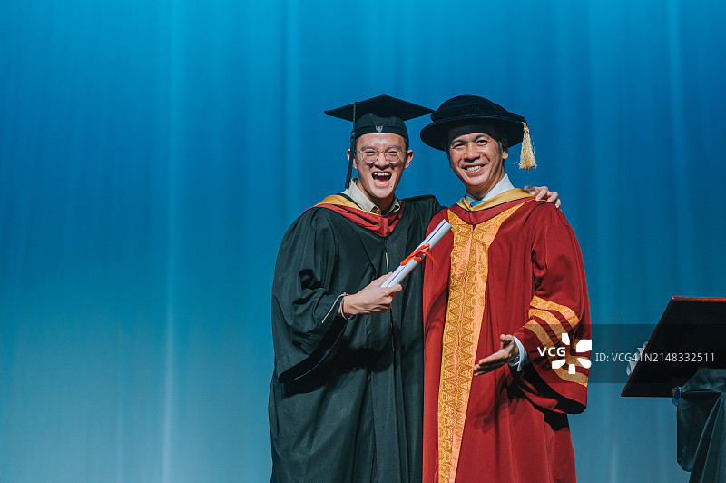 毕业典礼激动的亚洲毕业大学男学生在礼堂的舞台上接过毕业奖状后站在院长旁边图片素材