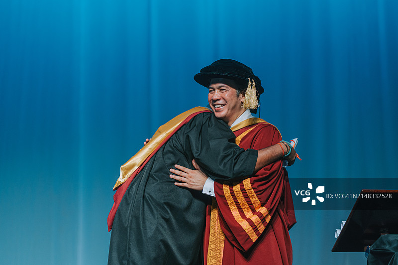 亚洲大学生在礼堂舞台上毕业，与院长拥抱图片素材