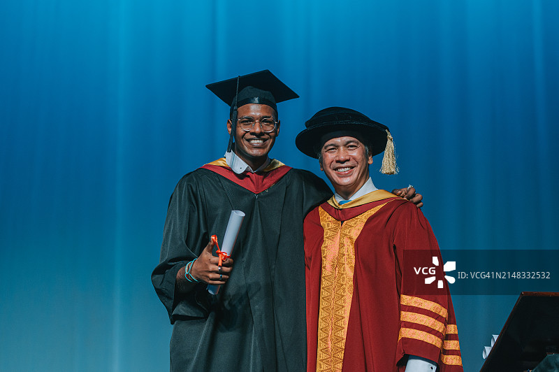 毕业典礼：印度裔男大学生在礼堂舞台上从院长手中接过毕业证书图片素材