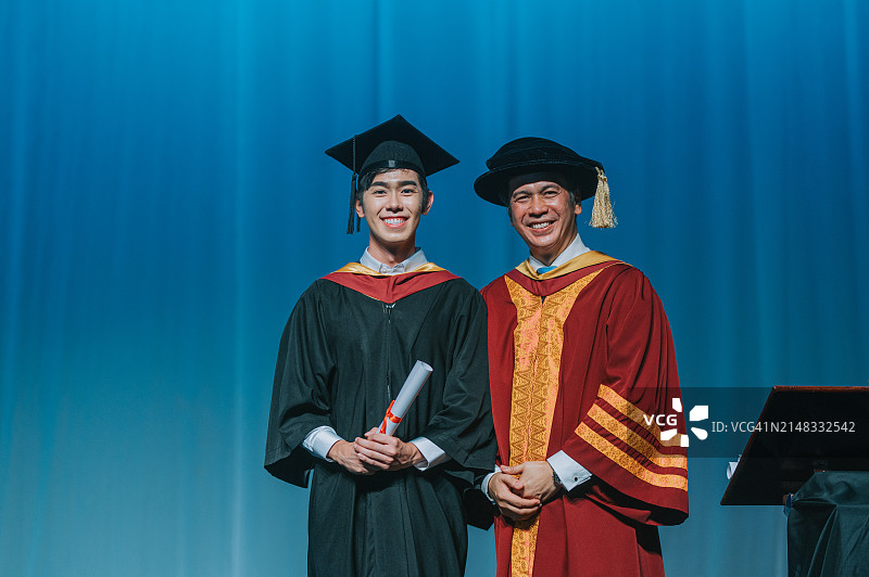 毕业典礼：亚洲学生在礼堂舞台上从院长手中接过毕业证书图片素材
