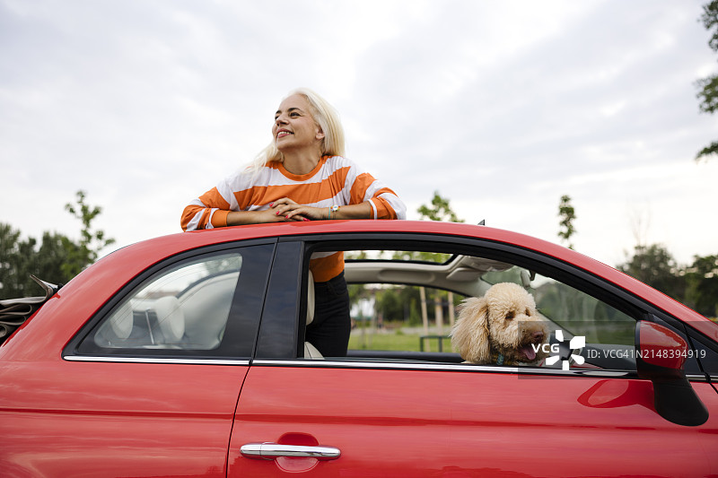 一位金发白人女子和她的狗在一起，透过汽车的天窗看着，用手指着狗图片素材