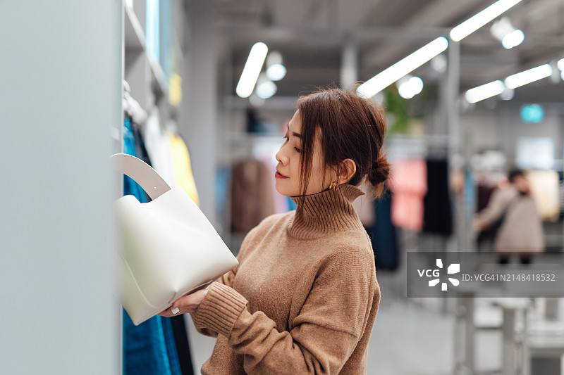 在服装店看手提包的亚洲年轻女人图片素材