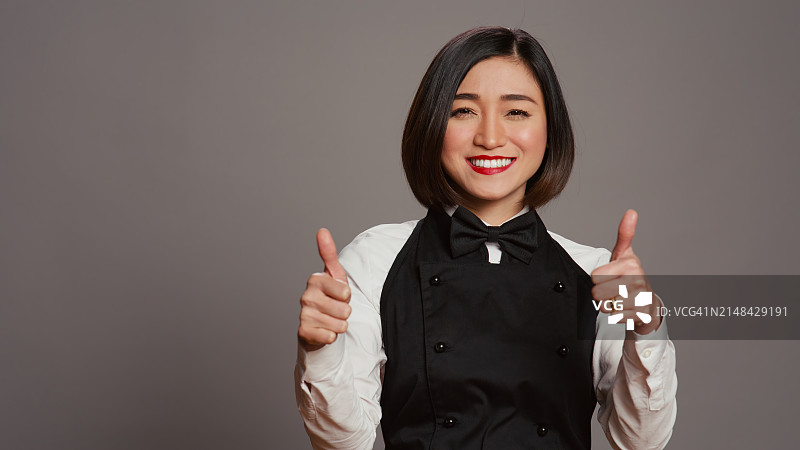 站在灰色背景前做手势的微笑年轻女人肖像图片素材