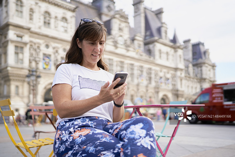 在户外咖啡馆使用手机查看社交媒体，发布度假照片的女人图片素材