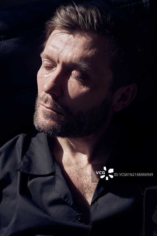 特写：一位穿着黑色衬衫的英俊男子坐在阳光下的皮椅上，男士美容概念图片素材