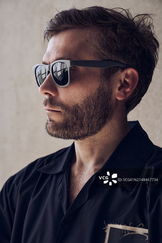 站在米色背景上的英俊男人头像，他穿着黑色衬衫和太阳镜。有胡子的男人，美容概念。图片素材