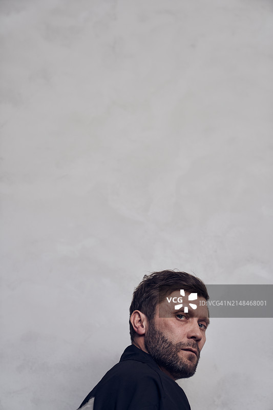 站在米色背景下的黑衬衫英俊男子头像。穿着时尚的胡须男士，后视图，带有复制空间图片素材