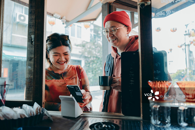 一名女子使用智能手机向收银员付款，她使用读卡器扫描二维码完成便捷的非接触式支付图片素材
