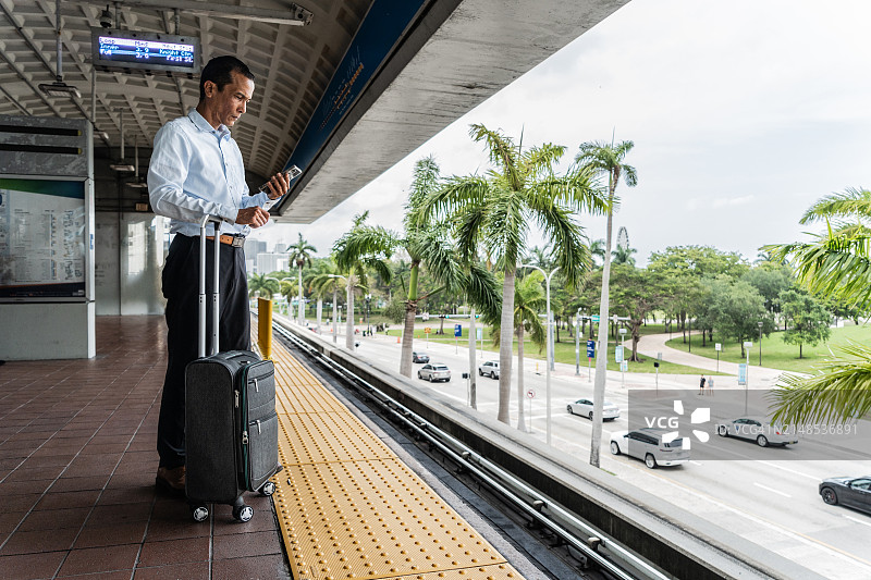 中年商人站在车站使用手机候车图片素材