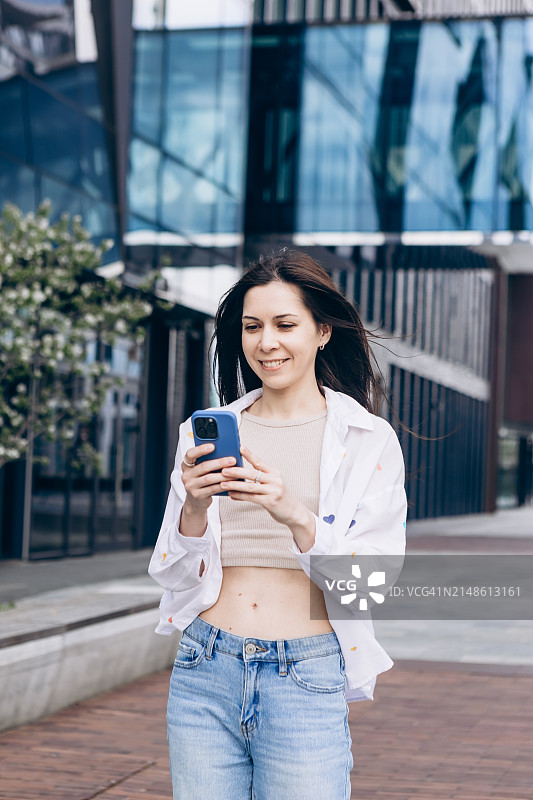 自信年轻棕发女人在城市用智能手机图片素材